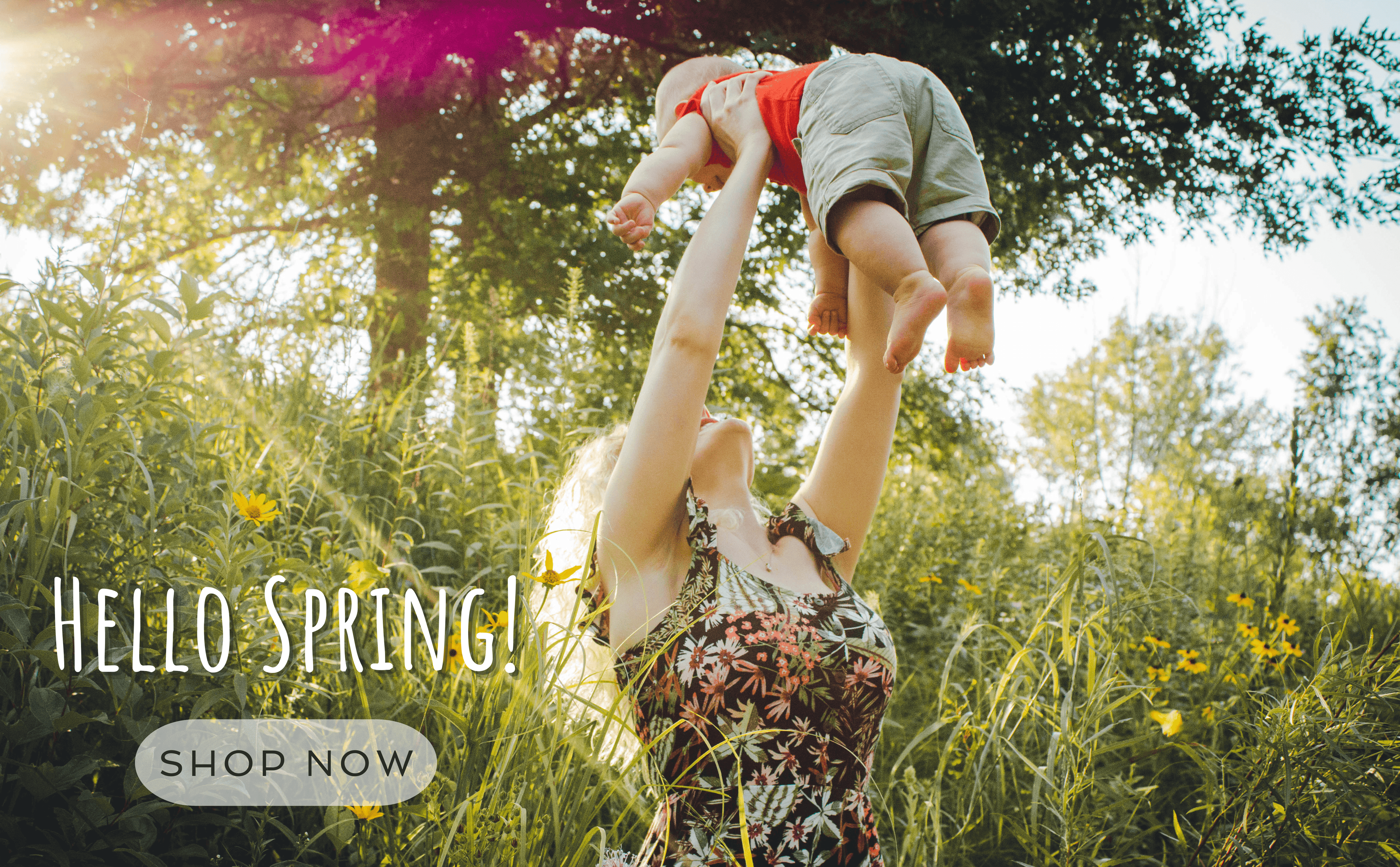 A smiling mother lifts her baby in a sunshine filled garden